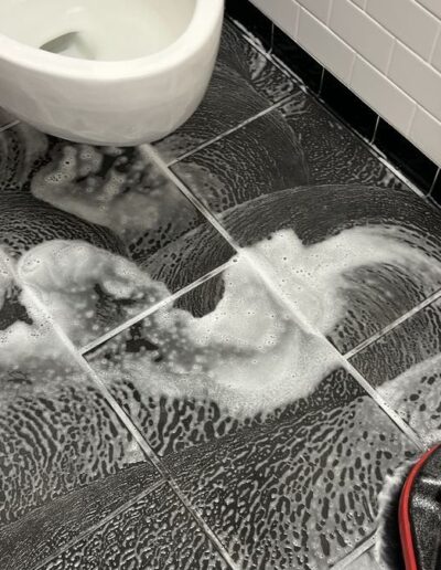 Close-up of bathroom tile floor being deep cleaned with a scrubbing machine and foaming cleaner