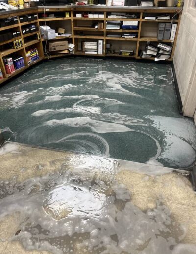 Green tile floor covered in cleaning foam in a storage room with supply shelving