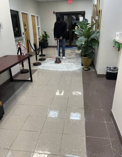 Worker operating a floor buffer machine to clean lobby tile floor near entrance doors