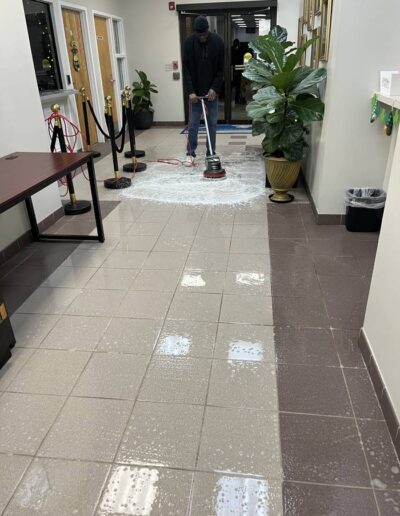Janitorial staff using a floor buffer to clean tile lobby floor near building entrance