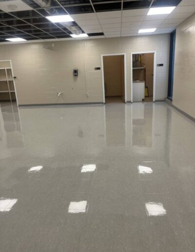 Glossy polished floor in an empty commercial room with a cleaning ladder and doors visible