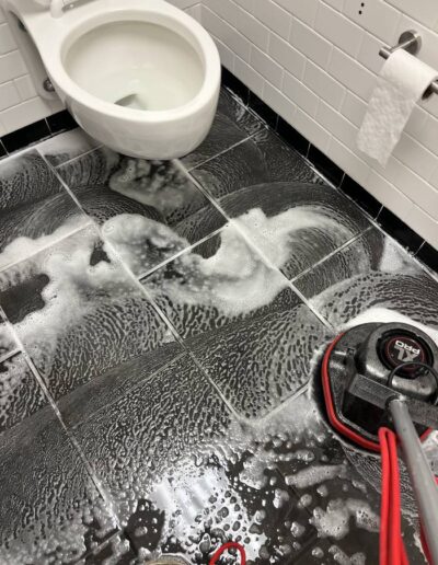 Bathroom tile floor being deep cleaned with a scrubbing machine and foaming cleaner